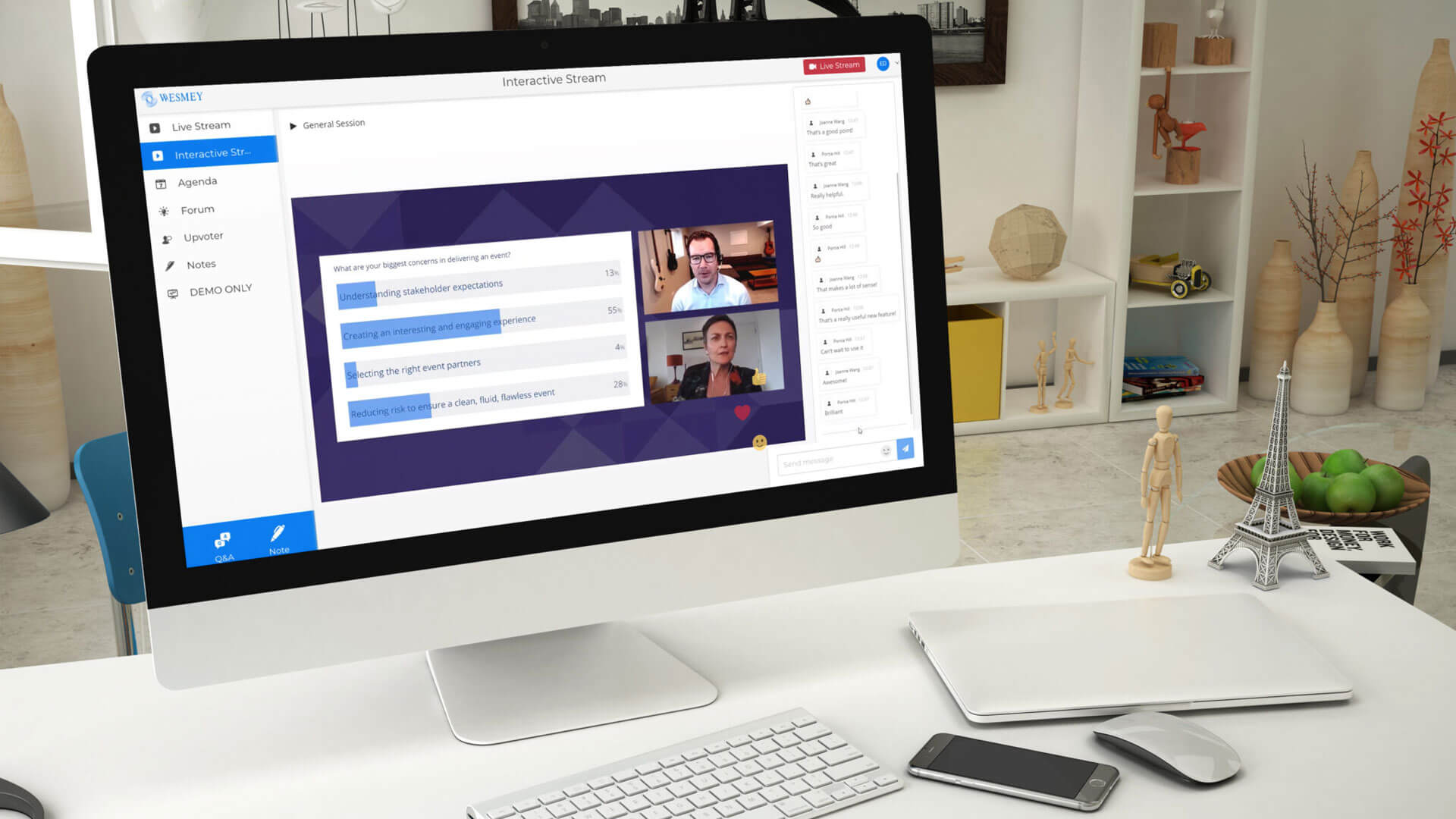 A computer monitor on a desk displays a virtual meeting with two participants and a shared screen. The desk has a keyboard, mouse, phone, notepad, and decorative items including a small Eiffel Tower model.