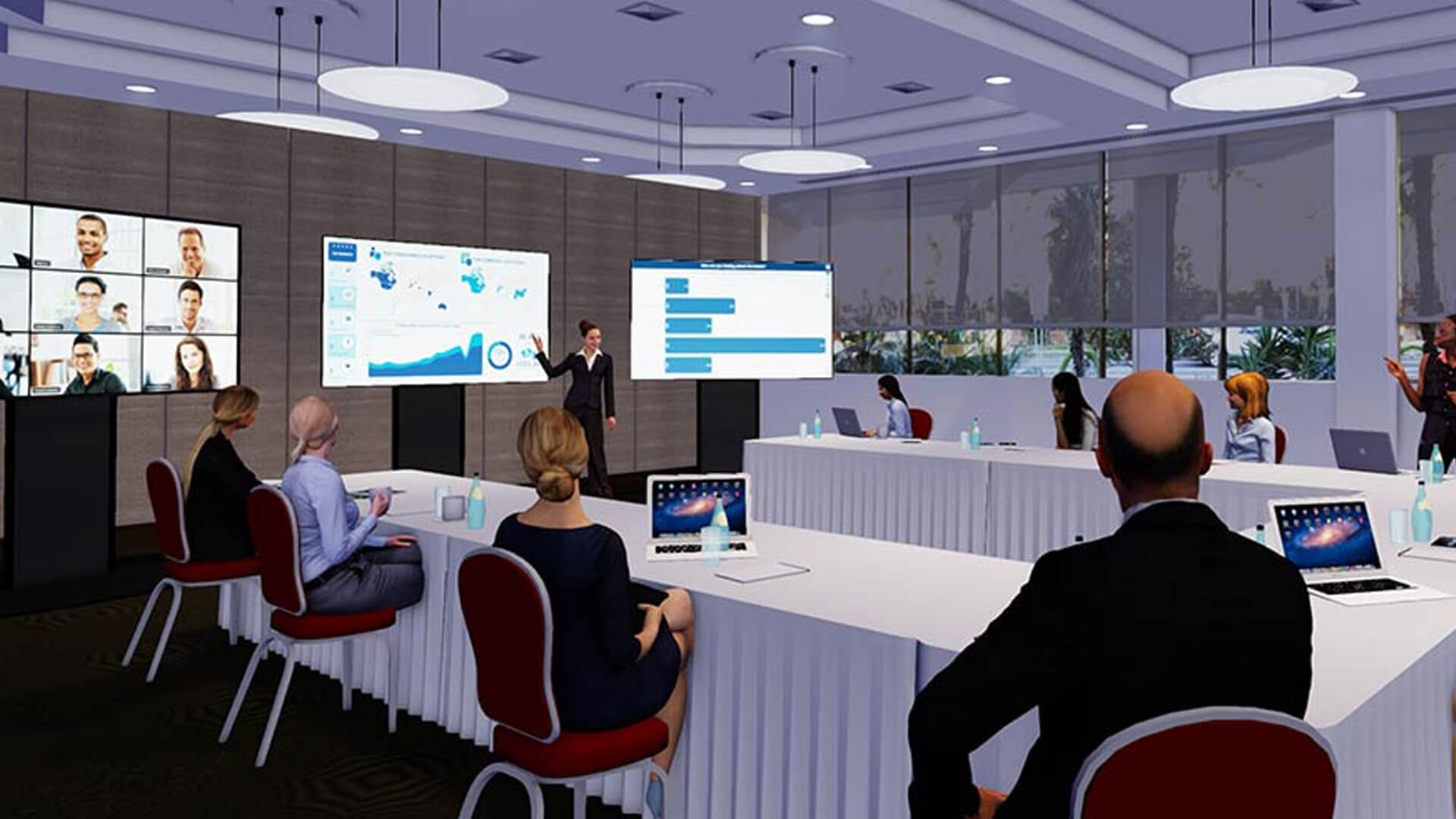 A modern conference room with people seated at tables, laptops open, watching a presenter explaining charts on large screens. Virtual participants are visible on video call monitors in the background.